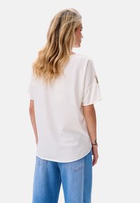 Witte T-shirt met korte mouwen van zachte stof, met een ronde halslijn en een relaxte pasvorm. De achterkant heeft subtiele logo-accenten.