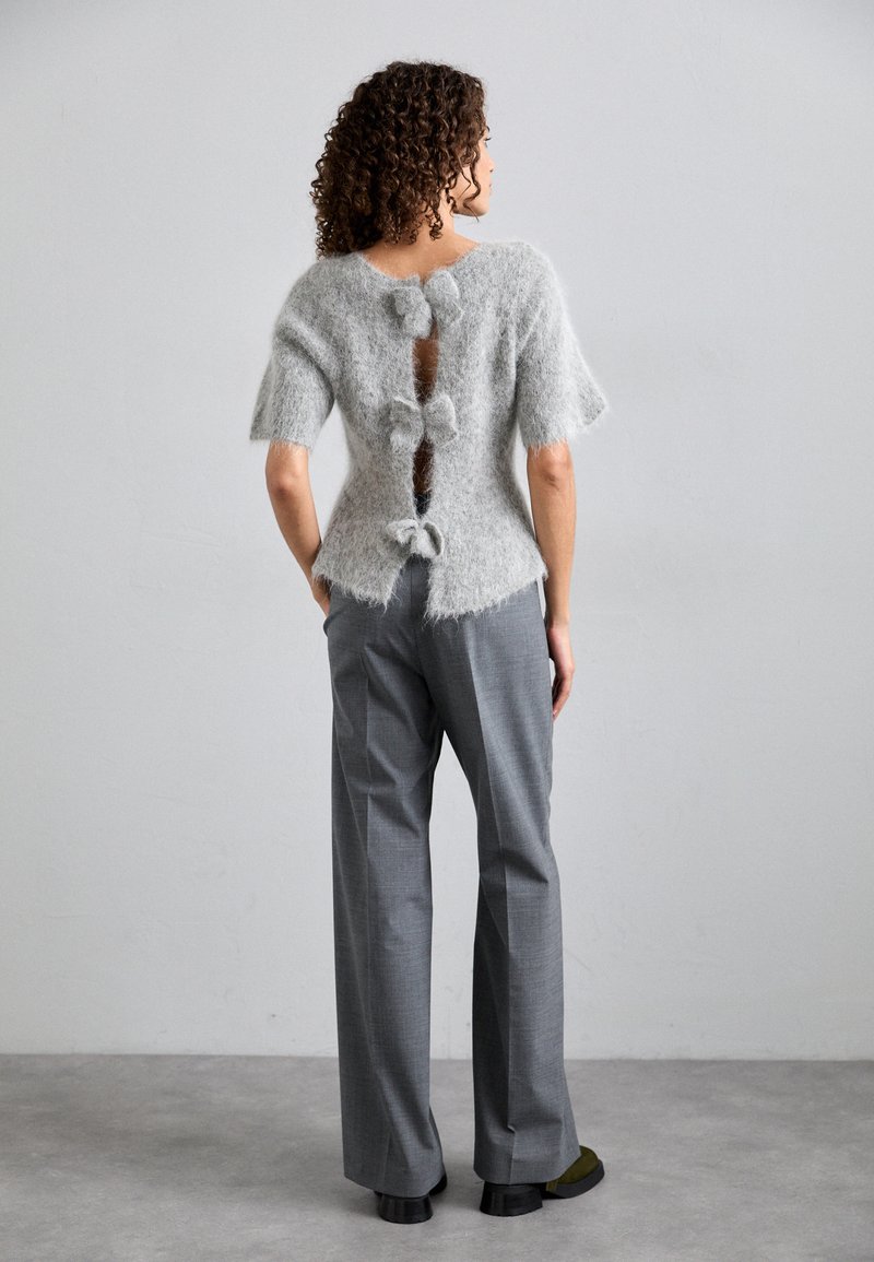 Γκρι πουλόβερ από μοχέρ με κοντά μανίκια και άνοιγμα στη�ν πλάτη, διακοσμημένο με τρεις κορδέλες από ύφασμα. Συνδυάζεται με γκρι παντελόνι με φαρδιές γραμμές.