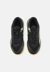 Chaussures de sport noires avec des panneaux en mesh, des accents verts et une semelle en caoutchouc texturée. Présente des lacets et un design moderne et épuré.