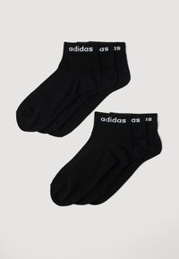 Calzini sportivi neri in cotone con logo "adidas" bianco sul polsino, caratterizzati da una texture liscia e altezza standard fino alla caviglia. Confezione da quattro.