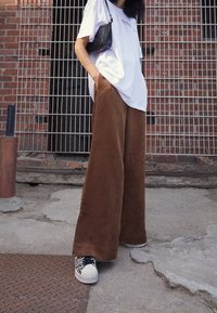 Szerokie brązowe spodnie sztruksowe, zestawione z luźną białą koszulką i wzorzystymi trampkami. Stylizacja uzupełniona małą czarną torebką.