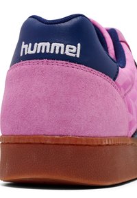 Talons de baskets en daim rose avec col en cuir bleu marine, broderie du logo "hummel" blanc et semelle extérieure en caoutchouc marron texturé.