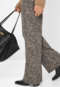 Pantaloni a gamba larga con stampa leopardata in toni terrosi smorzati, abbinati a una borsa in pelle nera con manici piatti e dettagli in oro.
