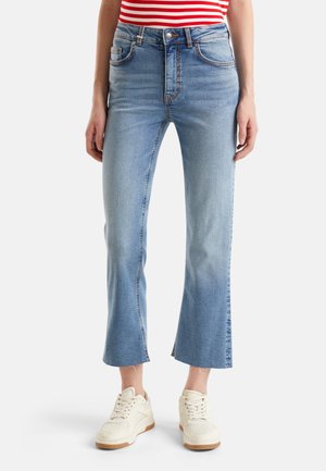 Jean en denim bleu clair avec taille haute, bas évasé et dégradé subtil. Comprend des poches standard et des détails de couture. Associé à des baskets blanches.