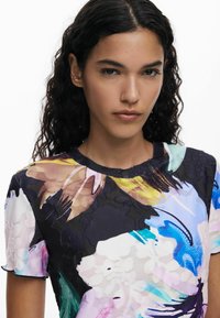 Top de manga corta con estampado floral que presenta una mezcla de colores vibrantes sobre un fondo oscuro, confeccionado en una tela suave con acabado texturizado.