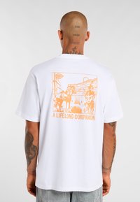 Bílý bavlněný tričko s velkým oranžovým grafickým designem zobrazením koní a osoby s kytarou, označené jako "CELOŽIVOTNÍ SPOLEČNÍK."