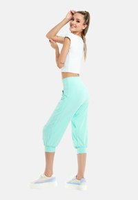 Top bianco leggero e corto abbinato a pantaloni verdi menta, a sigaretta, con polsini elasticizzati. Le scarpe sono sneakers nei toni pastello con una suola spessa.