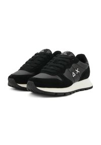 Zwarte en grijze sport sneakers met witte zolen, zwarte veters en witte symbolen aan de zijkanten, naast elkaar gepresenteerd op een witte achtergrond.