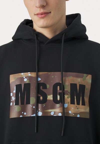 Schwarze Kapuzenjacke mit einem großen Grafikdruck, der die Buchstaben "MSGM" zeigt. Das Design hat Spritzer in Hellblau und Grün auf einem braunen Hintergrund.