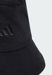 Zwarte bucket hat gemaakt van gestructureerde stof. Voorzien van een matte zwarte drie-strepen logo aan de voorkant. Brede rand voor bescherming tegen de zon.