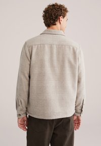 Helebeige ruuduline särgijope pehme tekstuuriga, nööpidega mansetid ja klassikaline krae, kantud tumeroheliste pükste peal.