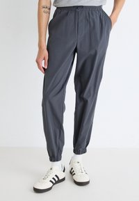 Pantalons de jogging gris légers avec une taille élastique, des jambes fuselées et des chevilles côtelées. Comprend des poches latérales et un design minimaliste.