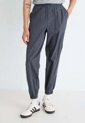 Lichte grijze joggerbroeken met een elastische tailleband, taps toelopende benen en opgerolde enkels. Voorzien van zijzakken en een minimalistisch ontwerp.