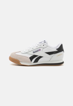 Zapatilla de cuero blanca con detalles en negro y acabado de ante. Presenta cierre de cordones, suela de goma y forro textil. Etiqueta "CAMPIO XT" en el talón.