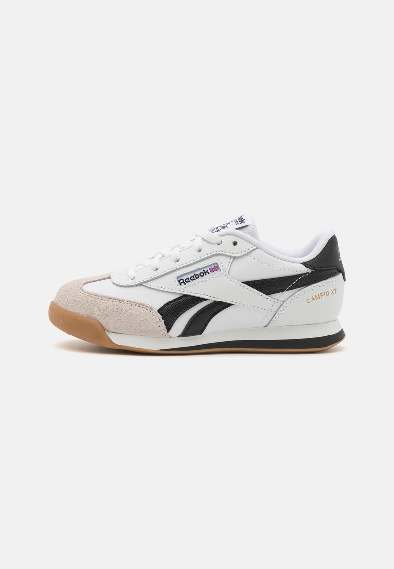 Hvite lær sneakers med svarte detaljer og semsket skinn. Har snøringslukking, gummisåle og tekstilforing. "CAMPIO XT"-merke på hælen.