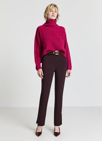 Flauschiger, knallpinker Rollkragenpullover mit gerippter Textur, kombiniert mit maßgeschneiderten, dunkelburgunderfarbenen Hosen mit einem seitlichen Schlitz und einem Gürtel.