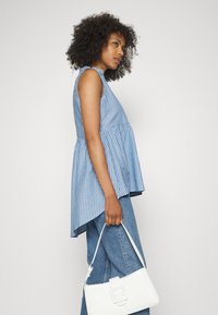 Top peplum à sem mangas, às riscas azul e branca, combinado com um jeans de cinta alta. A modelo segura uma pequena mala branca.