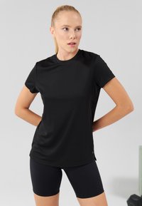 Tricou sport negru, confecționat dintr-un material neted și ușor, având guler rotund, mâneci scurte și un design ajustat. Asortat cu pantaloni scurți negri.