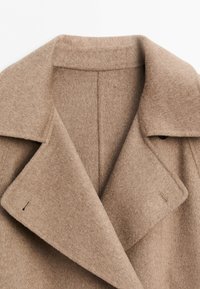 Beige wool coat collar with wide lapels and visible buttonholes, showing soft textured fabric and tailored seam details.