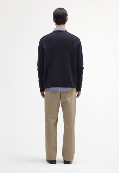 Granatowy sweter z dzianiny noszony na jasnoniebieską i białą koszulę w kratę, w połączeniu z beżowymi spodniami. Prosty wzór, brak wyróżniających się akcentów.