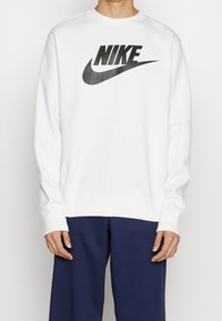 Vit Nike sweatshirt med en stor svart logotyp på framsidan, rund halsringning och långa ärmar. Tyget är mjukt med en avslappnad passform.