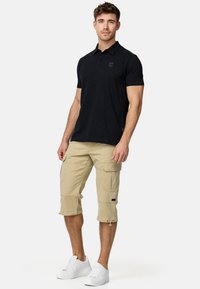 Sort polo shirt med krave, parret med beige cargo shorts med knælængde og lommer. Båret med hvide sneakers.
