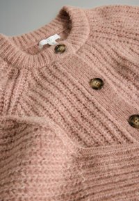Cardigan din amestec de lână, de culoare roz deschis, cu textură nervurată. Dispune de un decolteu rotund și doi nasturi maro. Aspect moale și confortabil.