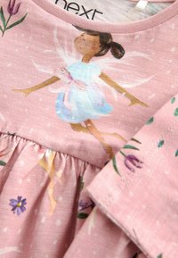 Rosa bomullsklänning med fladdrande ärmar, med en fe-tryck och blommiga mönster. Samlad midja och strukturerade tygdetaljer.