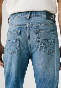 Svijetloplave traperice s opuštenim krojem. Imaju dva stražnja džepa; izvezeni logotip "Pepe Jeans London" na desnom džepu.