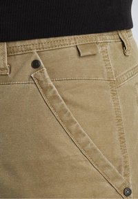 Beige denim shorts with visible stitching, button closure, and diagonal front pocket. Fabric has a smooth texture and a structured design.