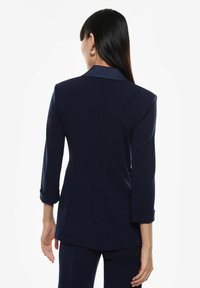 Blazer blu navy con design sartoriale, rever a punta e maniche 3/4. Texture morbida e vestibilità strutturata, con polsini arrotolati.