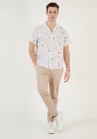 Korte mouwen witte shirt met een geometrische print in beige tinten. Gecombineerd met lichtbeige broeken en witte sneakers. Glad textuur.