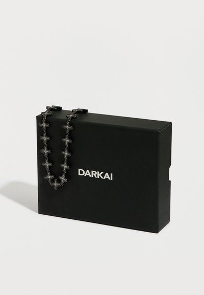 Fekete ajándékdoboz, rajta fehérrel a "DARKAI" márkanévvel, texturált nyaklánccal, amelyen fekete, kereszt alakú díszítések találhatók.