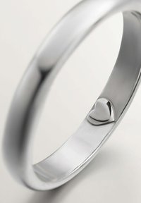 Anillo de metal plateado con una superficie lisa y pulida, con un pequeño detalle en forma de corazón en la banda interior.