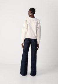 Felpa crema con design ricamato sulla parte posteriore, abbinata a jeans a gamba larga blu scuro. Tessuto morbido con dettagli a costine sui polsini e sull'orlo.