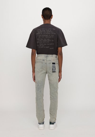 Czarna koszulka z nadrukiem na plecach, zestawiona z jasnoniebieskimi, znoszonymi dżinsami z naszywkami i ćwiekami. Białe trampki dopełniają look.