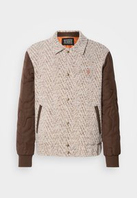 Giacca con bottoni, davanti in tessuto beige e marrone a trama, maniche trapuntate marroni scure, polsini a costine e due tasche anteriori.