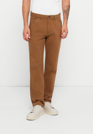 Brown straight-leg pants made of sturdy fabric, featuring a front button closure and side pockets, paired with light-colored sneakers.
