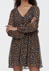 Robe fleurie avec une base bleu marine ornée de motifs floraux orange et bleus, décolleté en V, manches longues transparentes et taille cintrée.