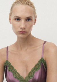 Camisole in raso lavanda con scollo a V profondo, caratterizzata da un intricato pizzo verde lungo il collo e spalline regolabili.