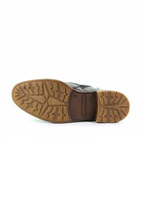 Brązowy skórzany but dressowy z podeszwą z teksturowanej gumy z wzorem w zygzak i zaokrąglonym czubkiem. Nazwa marki wytłoczona w pobliżu pięty.