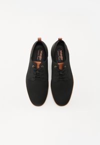 Juodi tinkliniai sportiniai bateliai su apvalia nosimi, rudomis detalėmis, auksinėmis akių anga ir paminkštintu padu. Yra traukimo kilpa ant kulno.