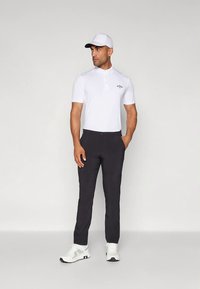 Λευκό κοντομάνικο πόλο πουκάμισο με γιακά, μαύρο παντελόνι και λευκά αθλητικά παπούτσια, ολοκληρωμένο με λευκό καπέλο. Απλός, καθαρός σχεδιασμός.