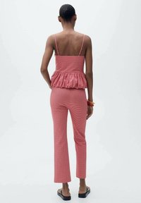 Rode geruite peplumtop met dunne bandjes, gecombineerd met bijpassende slim-fit broek. De set beschikt over een gestructureerde stof en een uitlopende broekspijp.