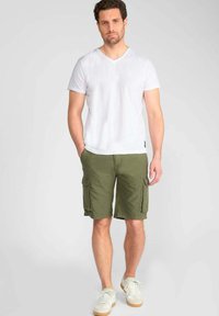 T-shirt blanc à col en V pour homme associé à un short cargo vert olive avec poches latérales, complété par des baskets légères. Tissu doux, coupe décontractée.