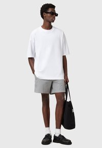 T-shirt bianca oversize, pantaloni corti a righe bianche e nere, occhiali da sole neri, scarpe nere e calze bianche. È portata una borsa tote nera.
