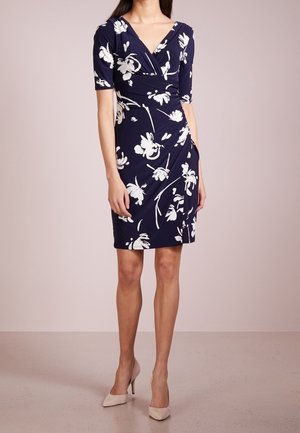 Granatowa sukienka w kwiaty z krótkimi rękawami, biały wzór kwiatowy, dopasowany fason, do kolan, gładki materiał. Noszona z cielistymi szpilkami.