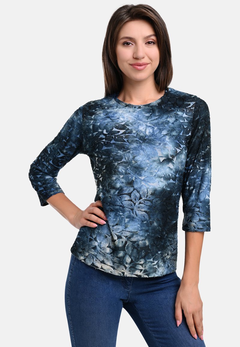Blue floral print long-sleeve top with a textured surface, featuring a round neckline and a fitted design, paired with dark jeans.