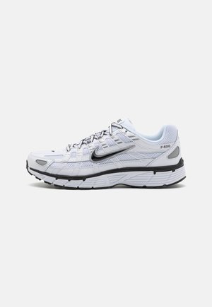 Baskets de course blanches avec une tige en mesh, bout arrondi, accents noirs et semelle à motif. Comprend des lacets et une marque sur le côté.