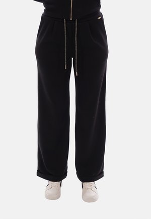 Pantaloni neri a taglio largo con vita e polsini con coulisse, indossati con sneakers casual bianche.